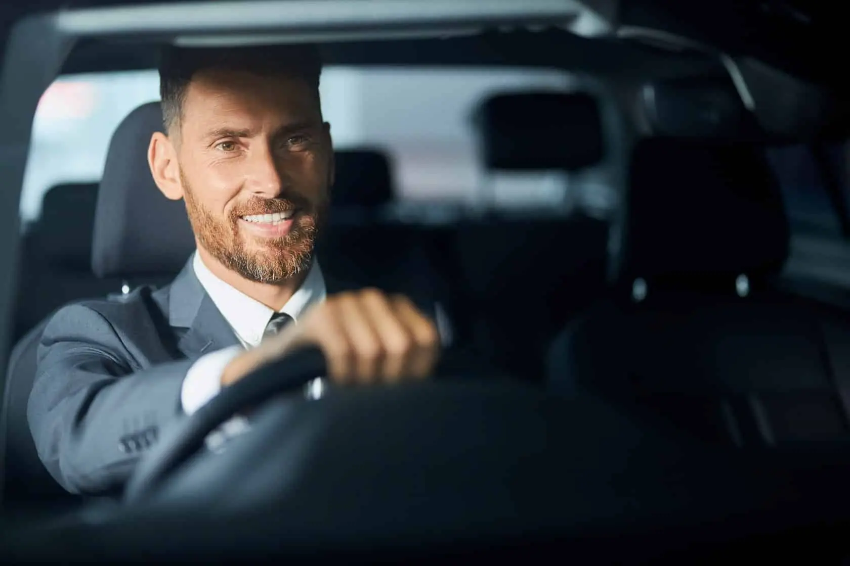 Chauffeur souriant portant un costume conduisant une voiture.
