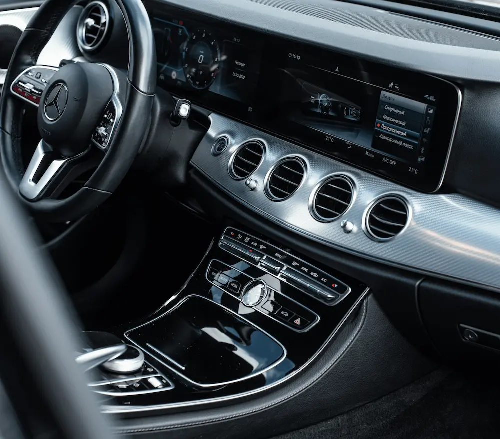 Intérieur moderne d'une voiture Mercedes avec volant multifonction, tableau de bord numérique large et sorties d'air circulaires.