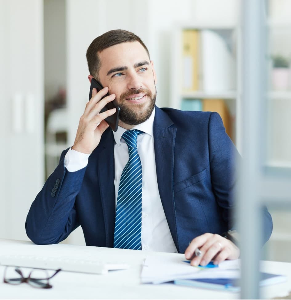 Homme d'affaires souriant en costume bleu parlant au téléphone dans un bureau moderne.