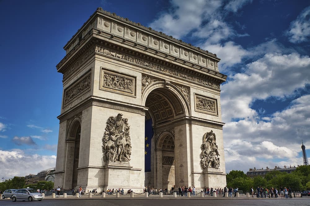 Arc de Triomphe à Paris sous un ciel partiellement nuageux avec des touristes autour.