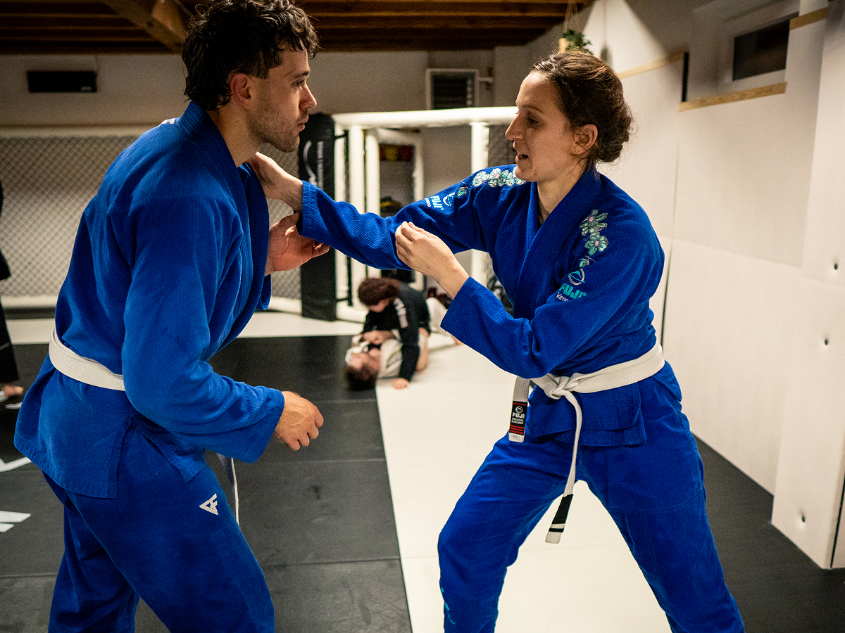 Eine Frau und ein Mann trainieren Brazilian Jiu Jitsu Techniken und Griffe im Anfängertraining.