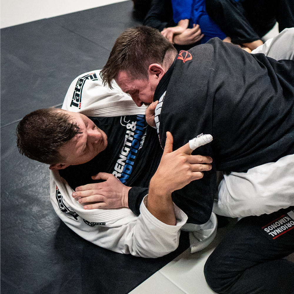 Zwei erfahrene Mitglieder trainieren Brazilian Jiu-Jitsu auf einer Matte mit Kimono.