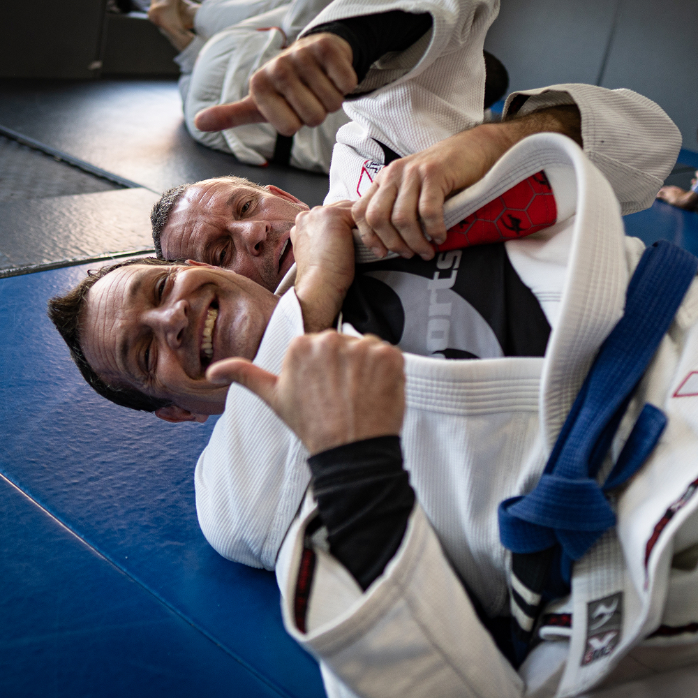 Zwei Männer trainieren gemeinsam Brazilian Jiu Jitsu und zeigen ihre Zufriedenheit mit einem Daumen nach oben.