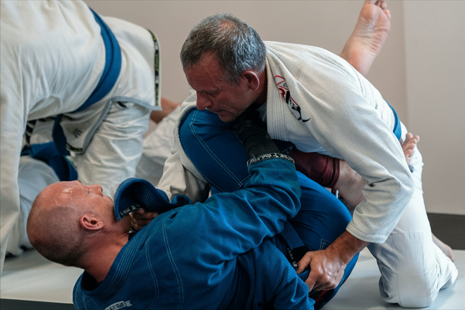 Zwei Männer trainieren Brazilian Jiu-Jitsu in weißen und blauen Gi-Anzügen auf der Matte.
