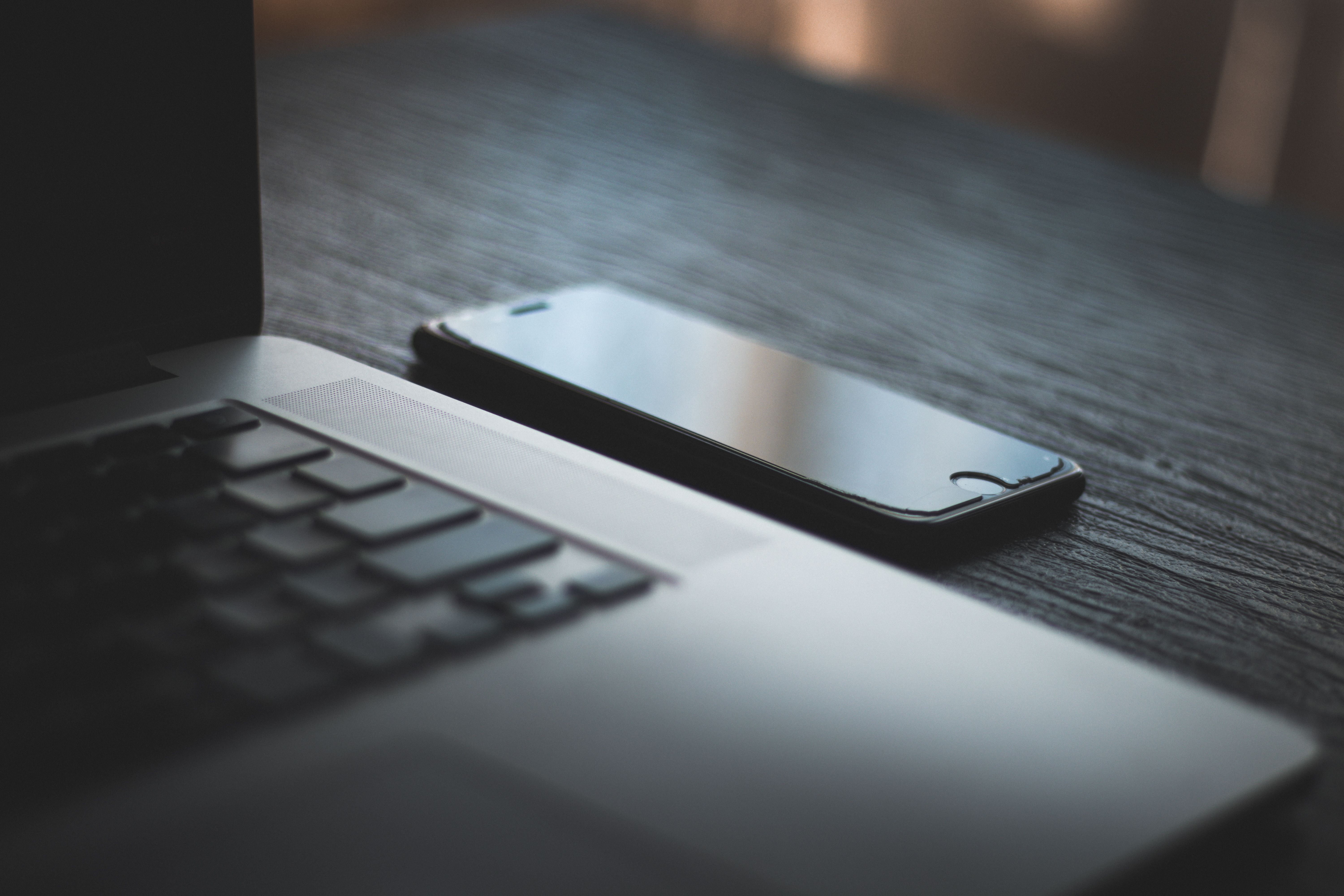 Smartphone lying next to a laptop keyboard on a dark wooden surface.