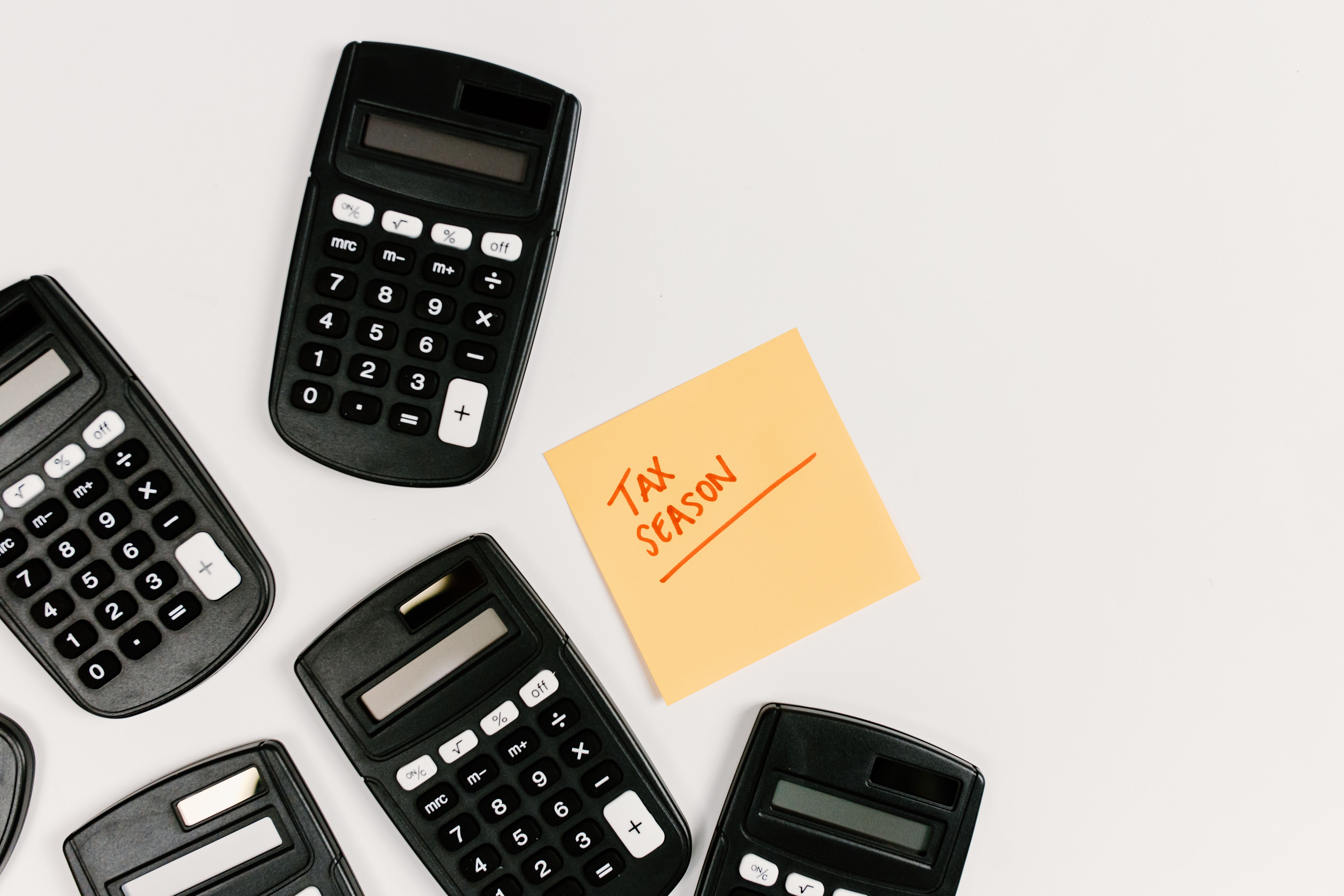 Several black calculators surrounding a yellow sticky note with Tax Season written in red.