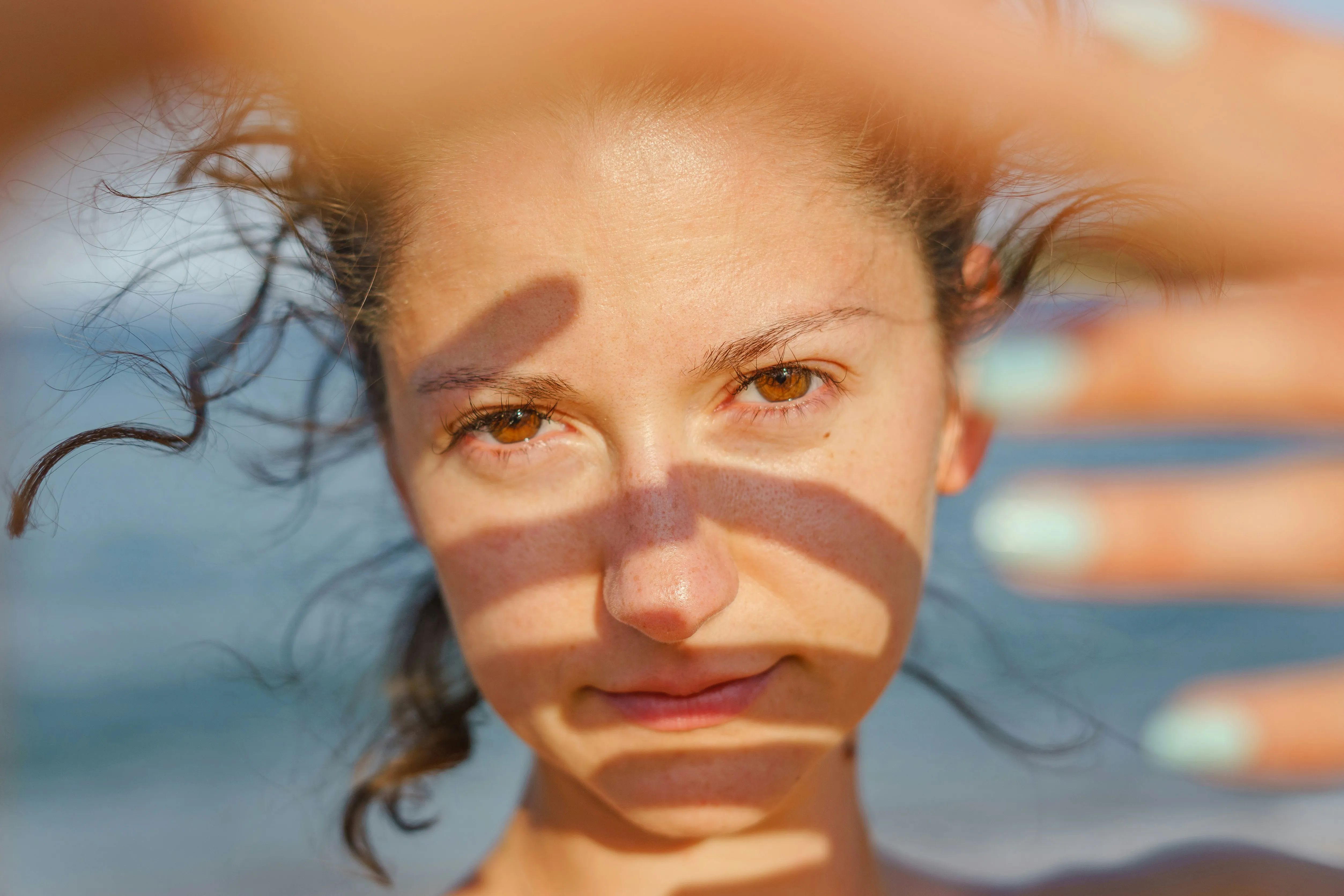 Woman shielding her face from sunlight to help prevent sun damage and premature skin aging