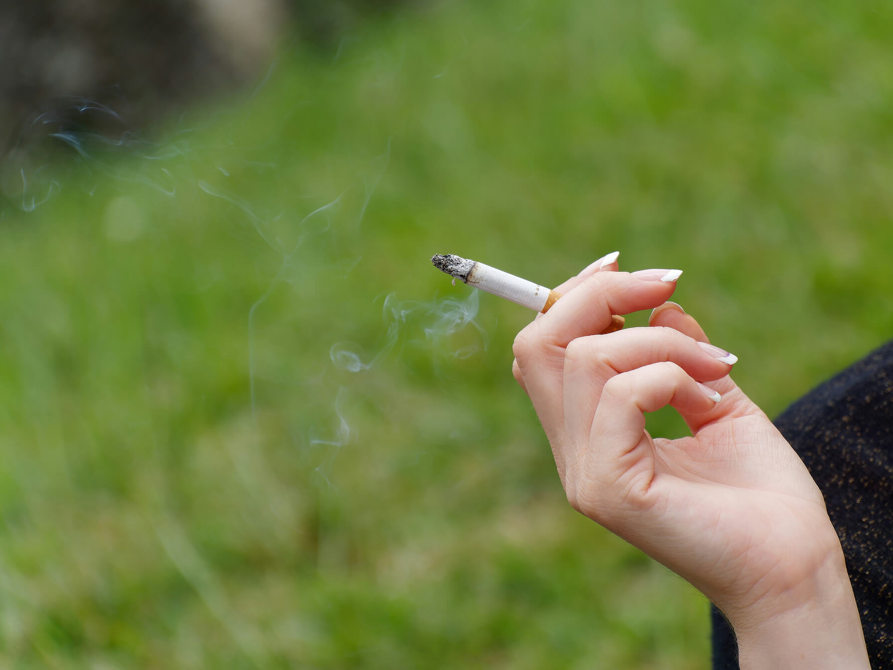 Close-up of a person holding a cigarette, illustrating how smoking accelerates skin aging and contributes to fine lines.