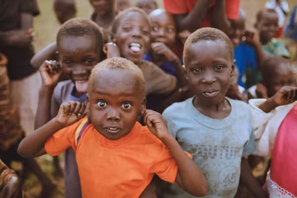 Group of children smiling and making playful faces outdoors, with one child in an orange shirt front and center.