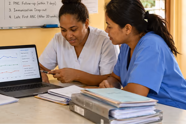 Two healthcare workers reviewing data on a laptop with medical files on the table in a clinic.