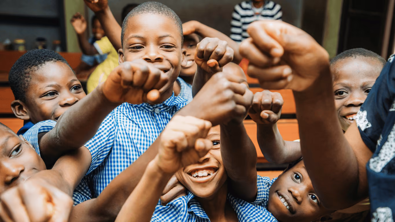 Group of smiling children in blue checkered shirts showing fists to the camera indoors.