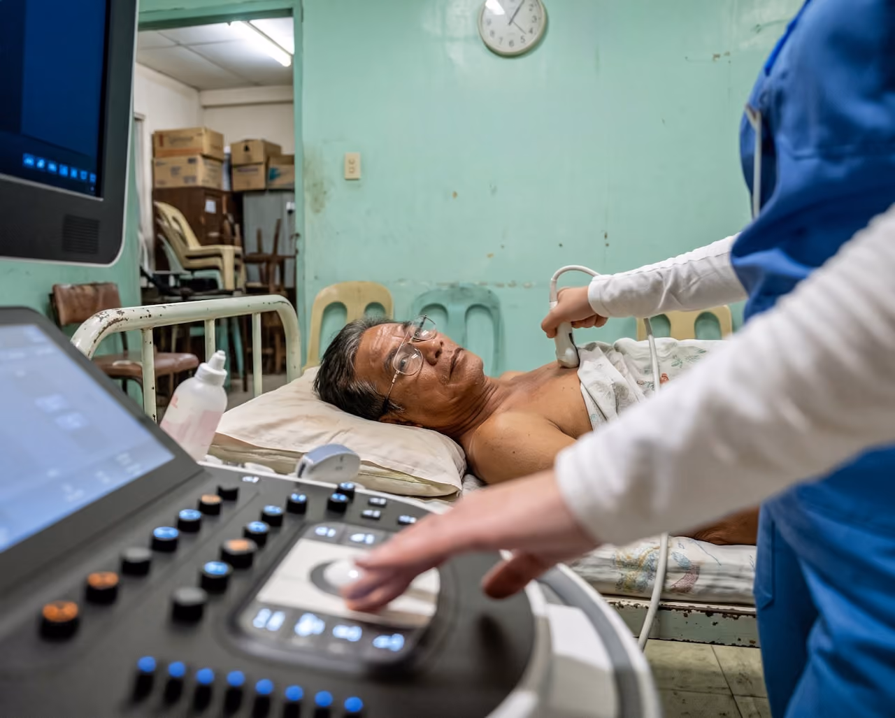 Patient lying on medical bed getting an echocardiogram ultrasound on chest by a healthcare worker.