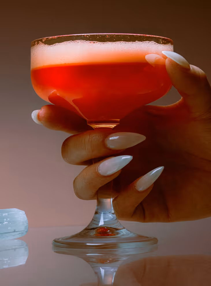 Image from Death to Stock - Hand with long nails holding a coupe glass filled with a red cocktail and foam on top.
