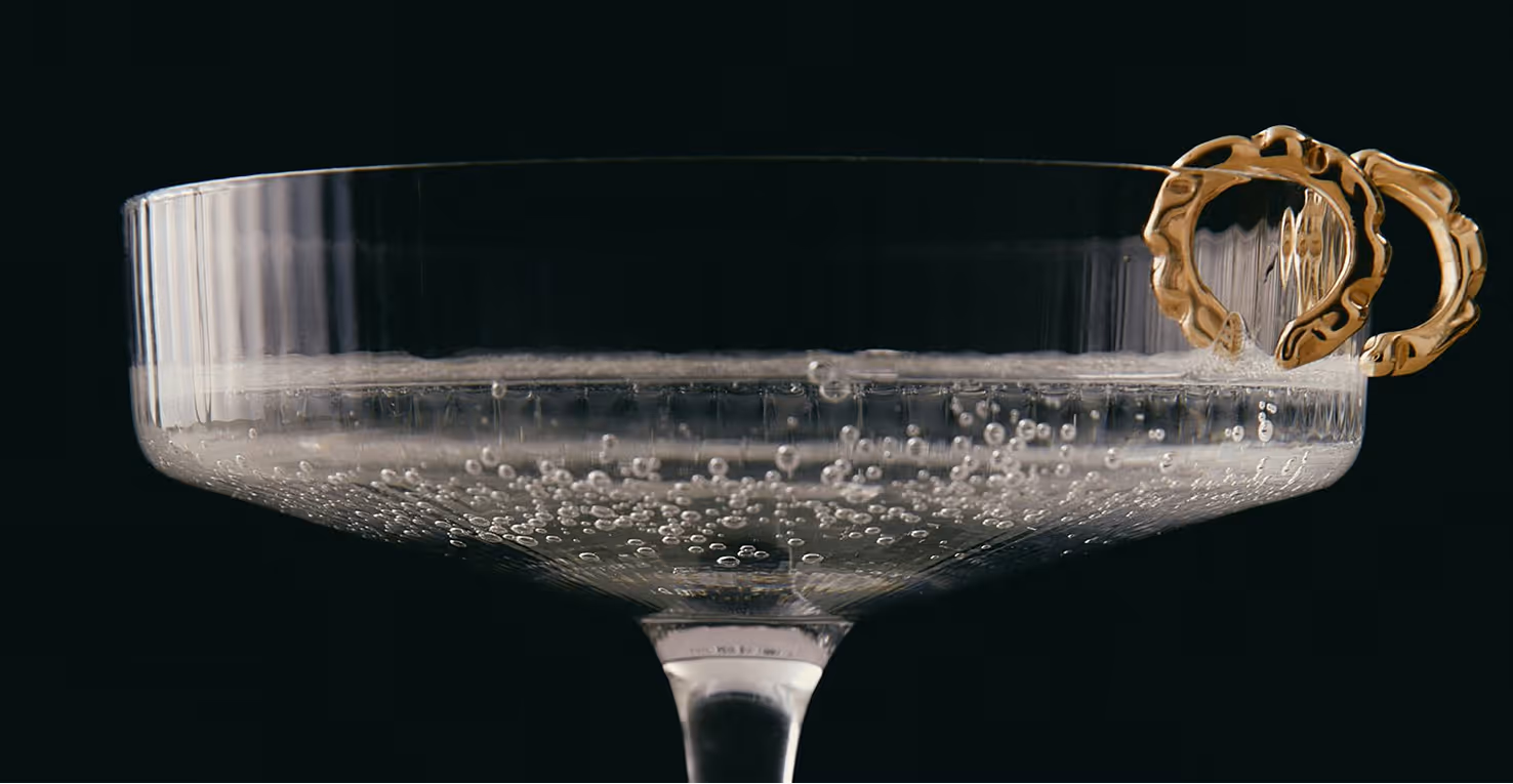 Image from Death to Stock - Close-up of a glass coupe filled with a bubbly clear drink and adorned with two decorative gold rings.