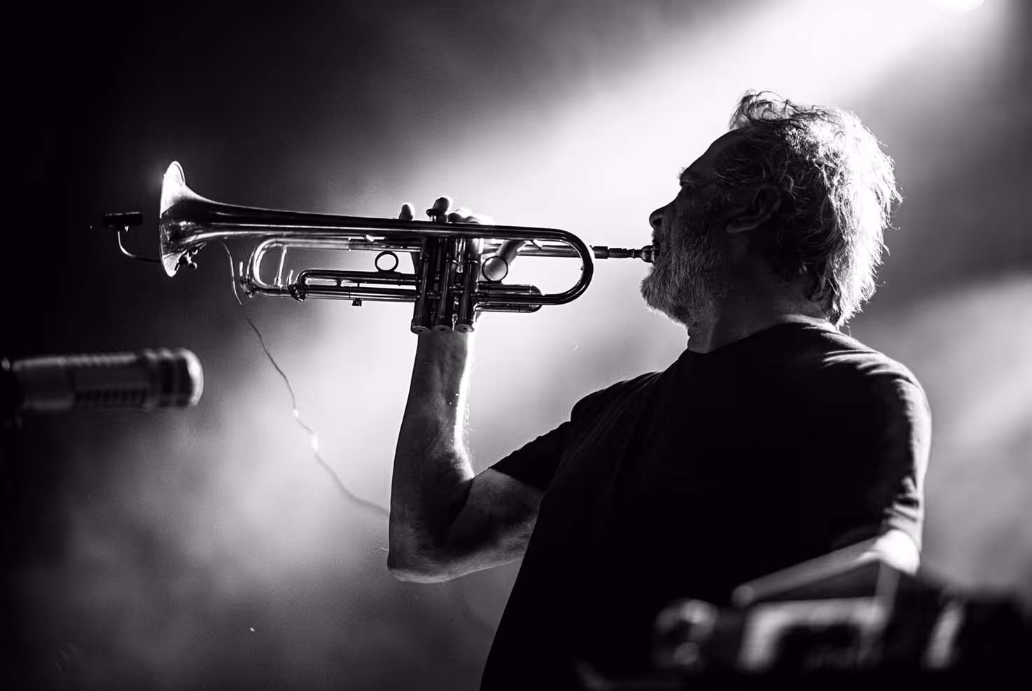 Photographed by Sławek Przerwa - Black and white photo of a man playing trumpet on stage with spotlight behind him.