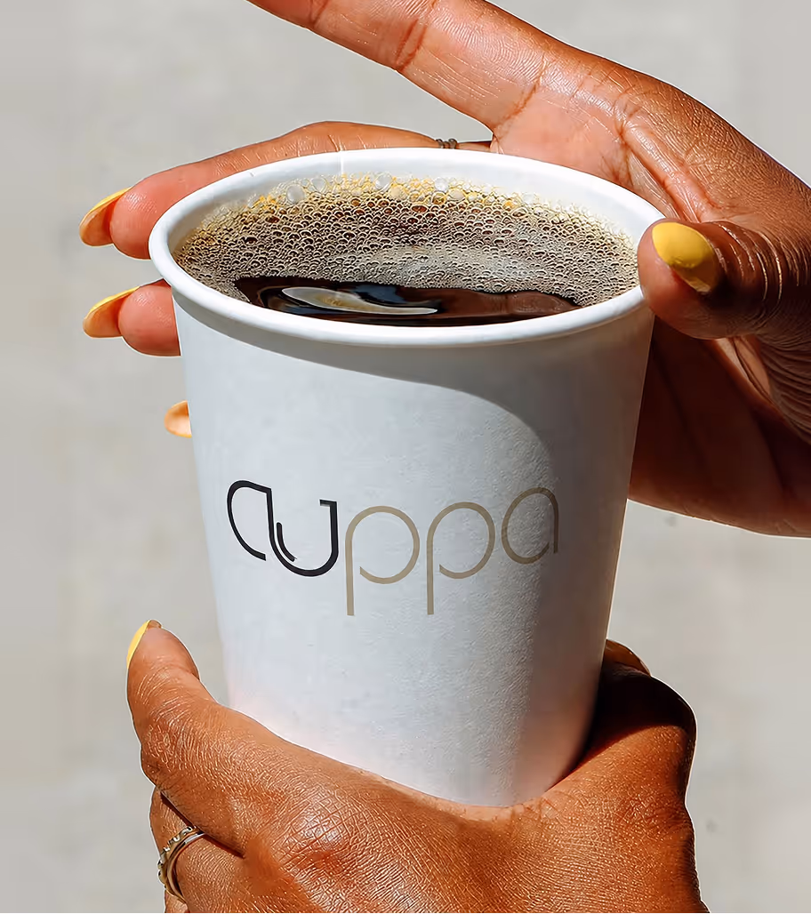 AI Generated image with ChatGpt - Hands with yellow nail polish holding a white paper cup labeled 'cuppa' filled with coffee.