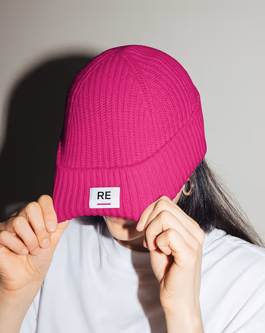 Mockup from Maison Mockup - Person wearing bright pink knit beanie covering face with hands, wearing white shirt and hoop earring.