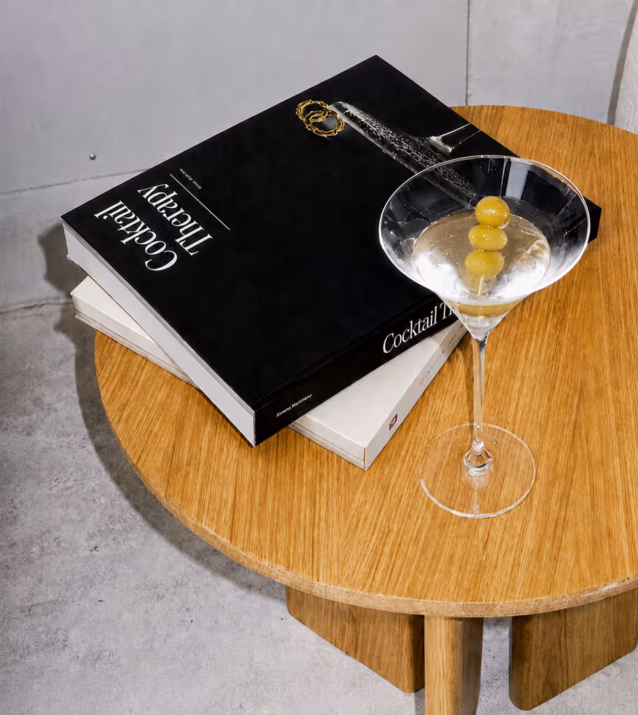 AI Generated image with ChatGpt - Martini glass with three olives on a wooden table beside two cocktail books, one titled Cocktail Therapy.