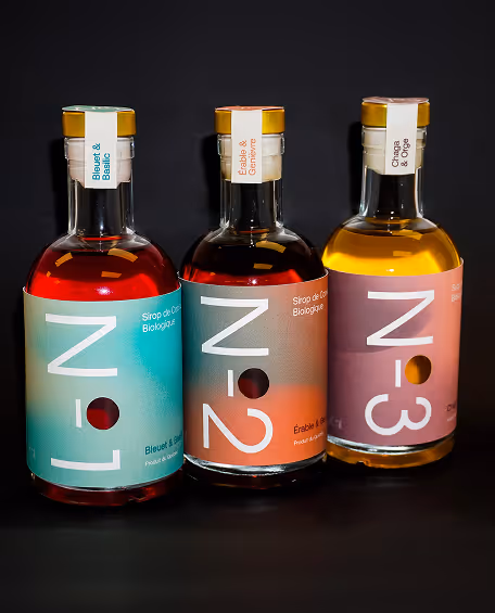 Photographed by Xhalia Martineau - Three bottles of organic syrup labeled N-1, N-2, and N-3 with different flavors on a black background.