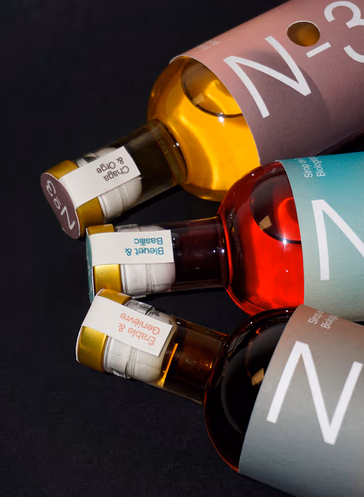 Photographed by Xhalia Martineau - Three glass bottles with colorful labels and scents: Chaga & Oige, Bleuet & Basilic, Erable & Genièvre.