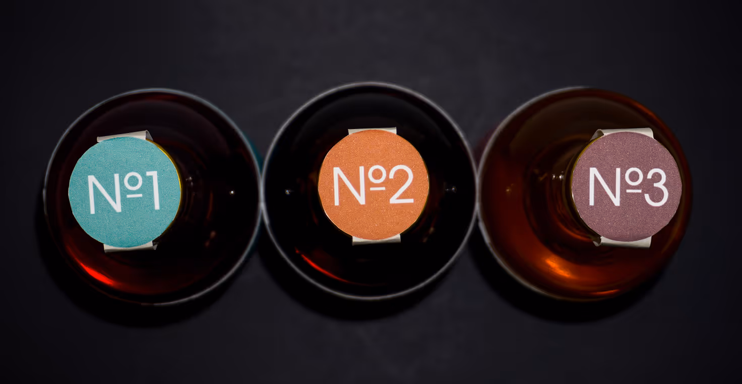 Photographed by Xhalia Martineau - Top view of three bottles with caps labeled No 1, No 2, and No 3 in teal, orange, and purple.