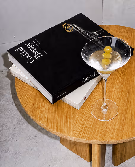 AI Generated image by ChatGpt - Cocktail glass with three green olives on a wooden table beside two stacked books.
