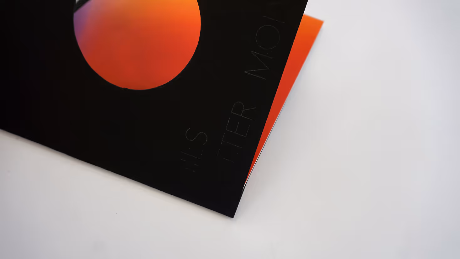 Photographed by Xhalia Martineau - Black vinyl record cover with an orange circle design on a white surface.