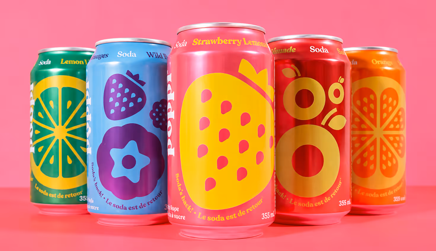 Photographed by Xhalia Martineau - Five colorful soda cans with fruit illustrations lined up against a pink background.