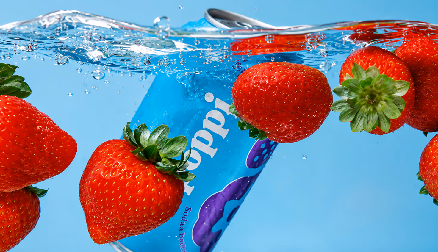 Photographed by Xhalia Martineau - Blue can submerged in water among floating red strawberries with green leaves.