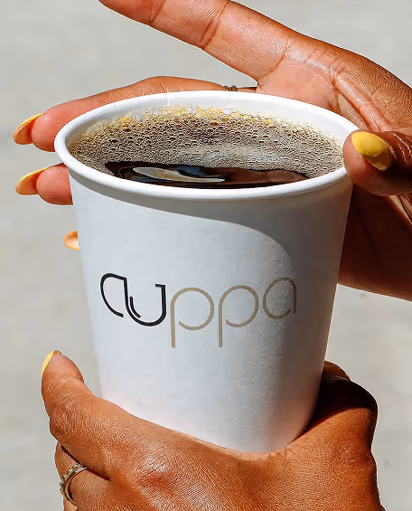 AI Generated image with ChatGpt - Hands with yellow nail polish holding a white cup of black coffee with 'cuppa' logo.