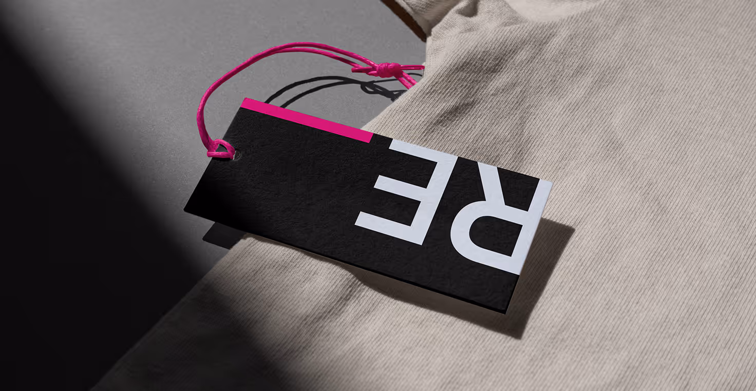 Mockup from Maison Mockup - Black and pink clothing tag with white 'RE' letters attached to beige fabric.