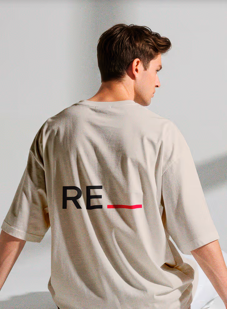 Mockup from Unblast - Man facing away wearing beige shirt with black 'RE' and red underline on the back.