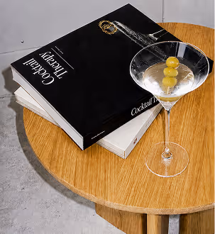 AI Generated image with ChatGpt - Martini glass with three olives beside two cocktail recipe books on a round wooden table.