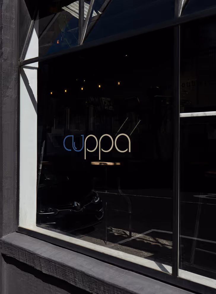 Mockup from Maison Mockup - Window with the word 'cuppa' in blue and white letters and reflection of street and lights.
