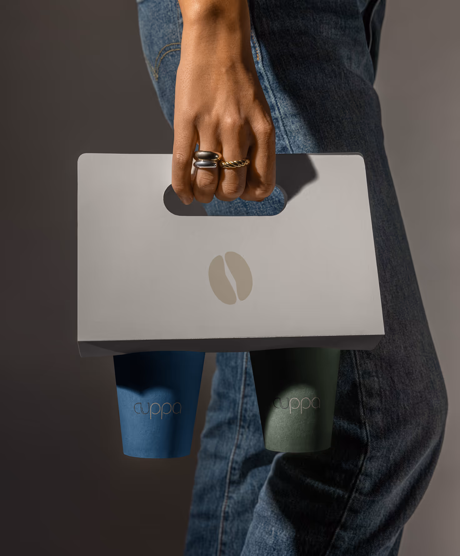 Mockup from Maison Mockup - Hand with rings holding a gray cup carrier with two disposable cups labeled 'cuppa'.