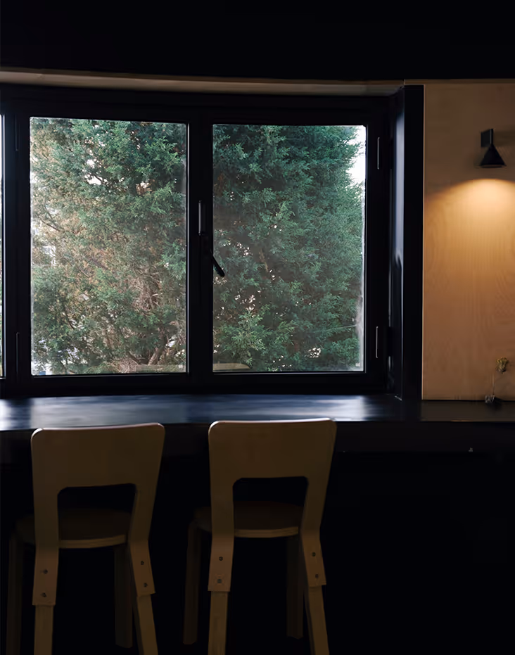 Two wooden chairs at a dark counter in front of a window with green trees outside.
