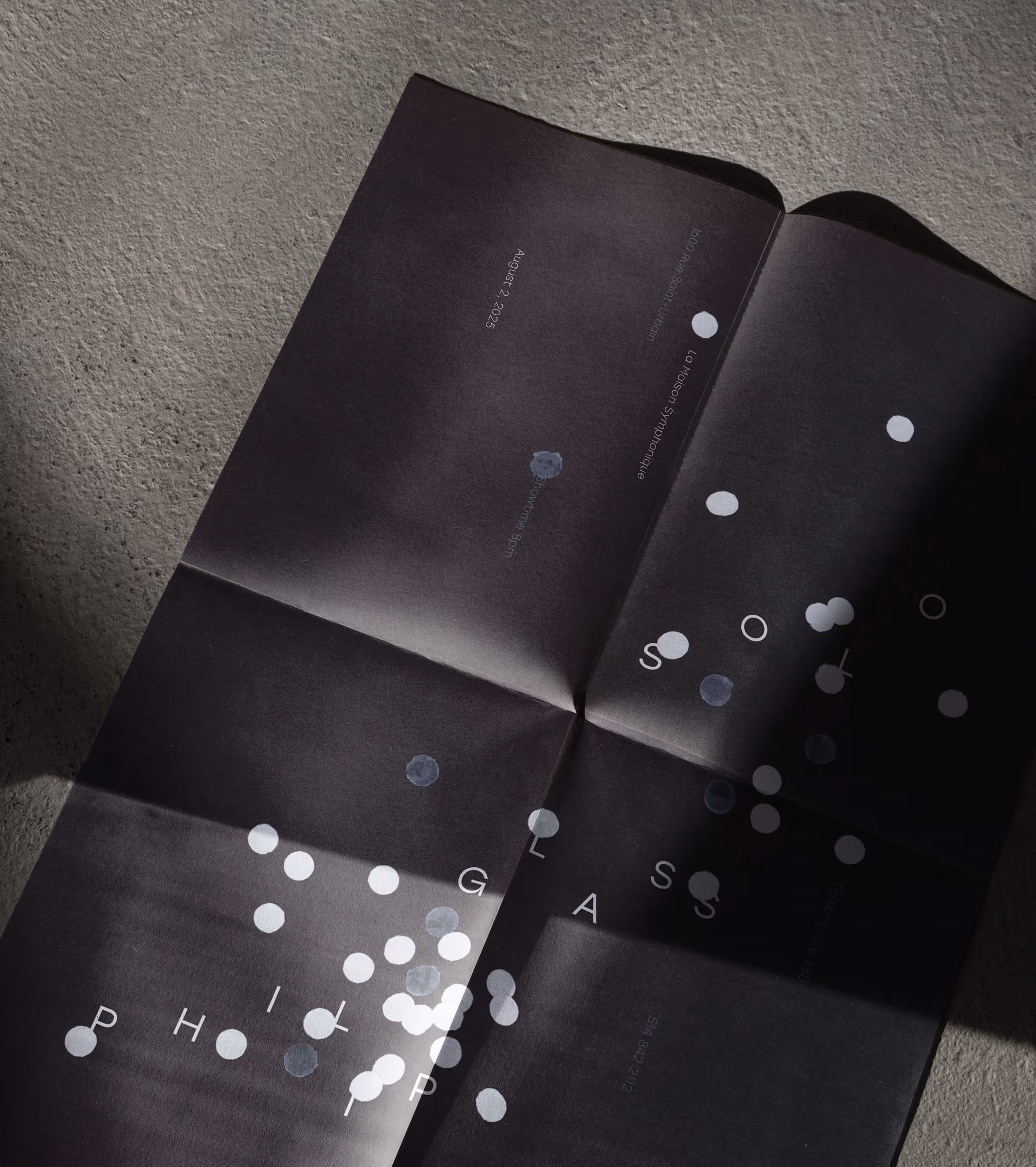 Folded black poster with scattered white dots and text on a textured surface with shadows.