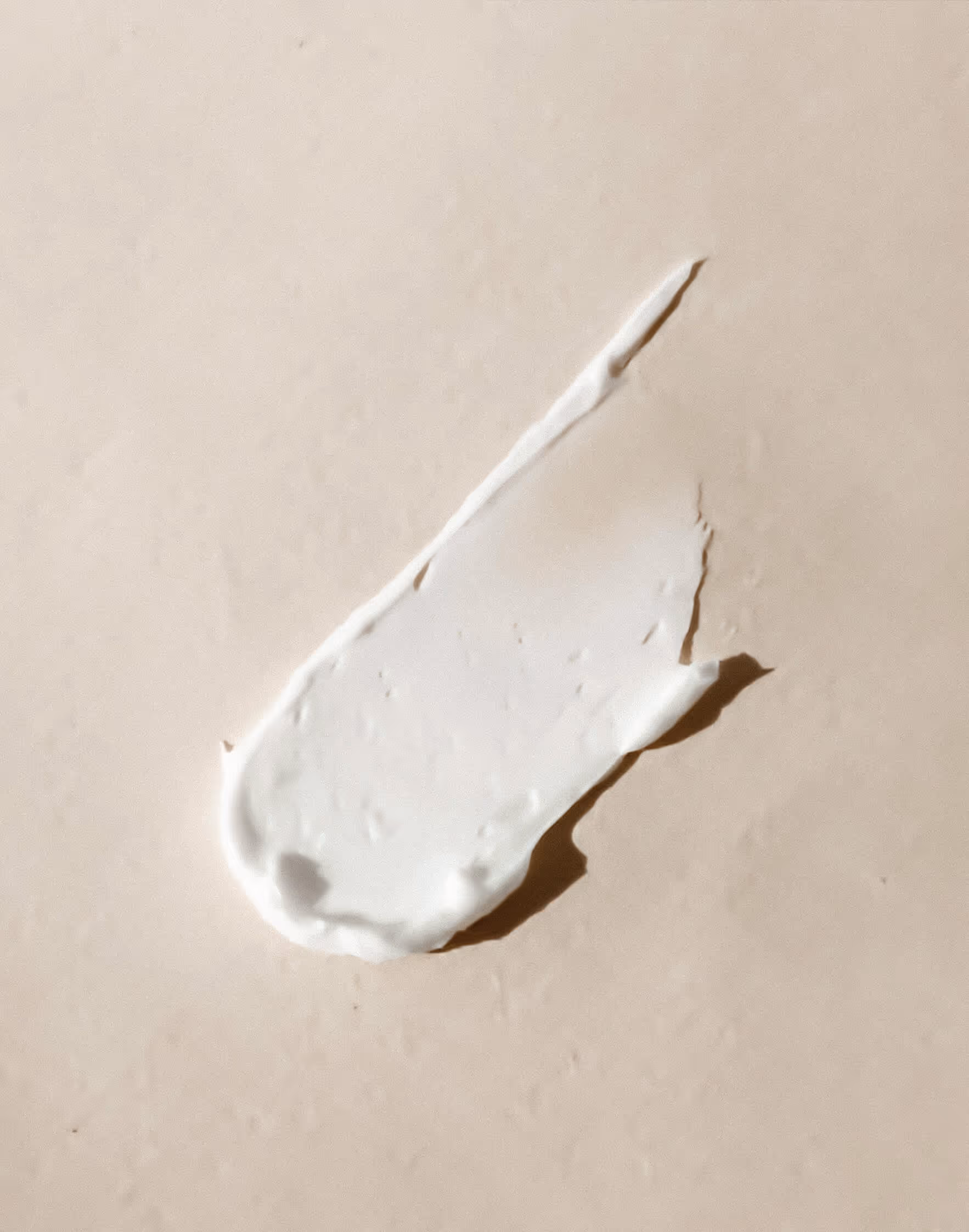 Smear of white cream or lotion on a beige surface.