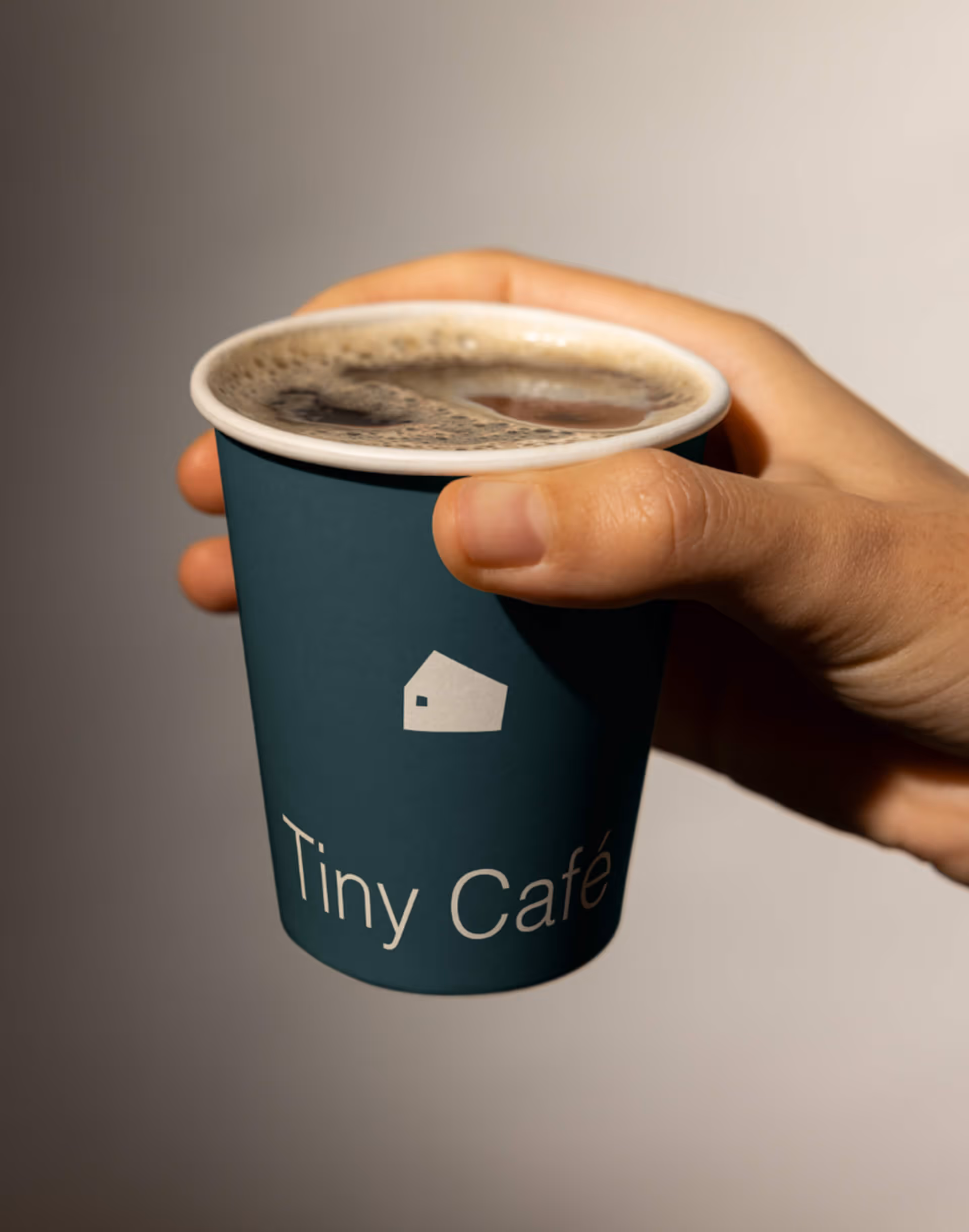 Hand holding a blue disposable cup of coffee with Tiny Café logo and foam on top.