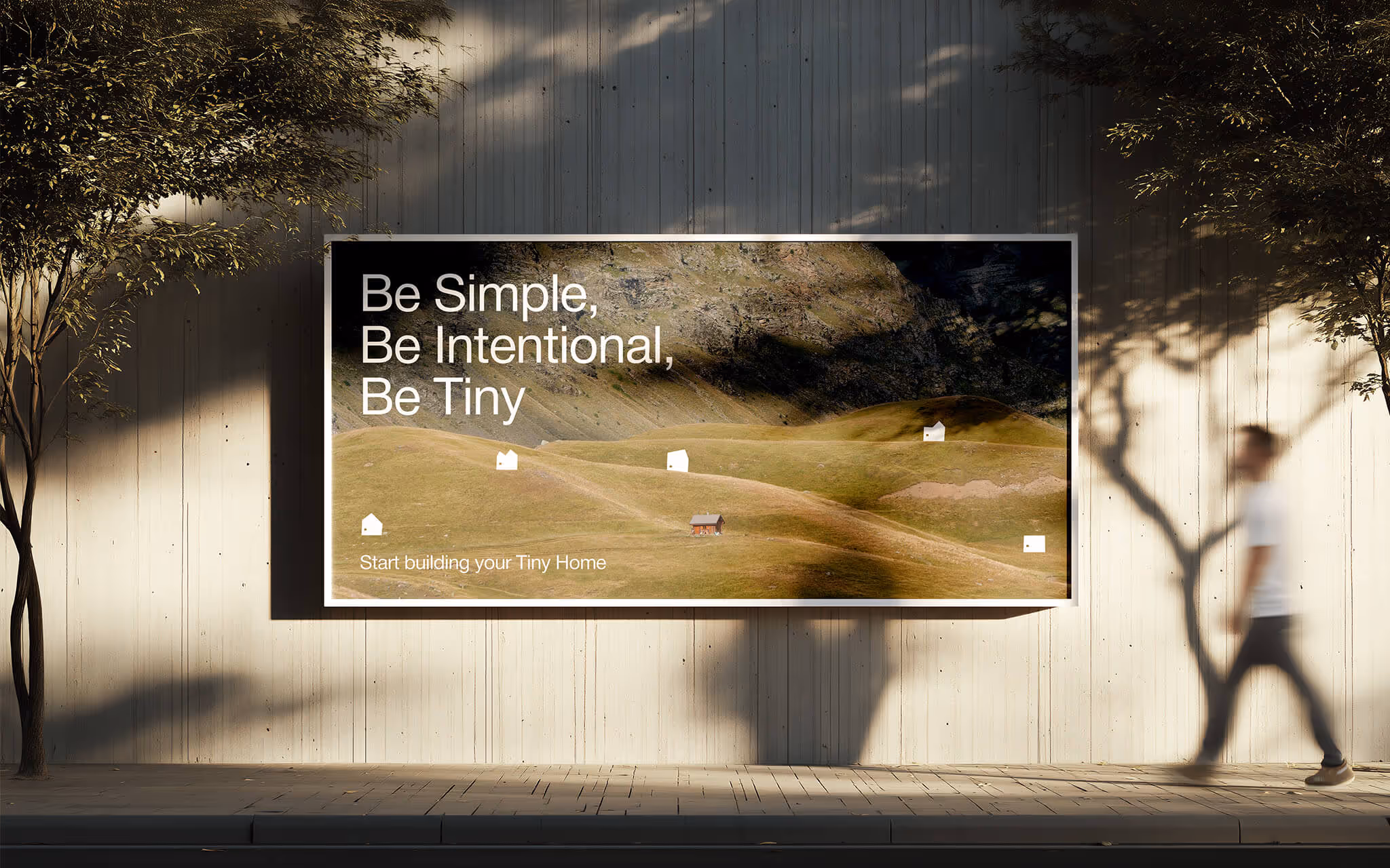 Outdoor billboard on a wall reads, 'Be Simple, Be Intentional, Be Tiny' with hilly landscape and tiny houses.