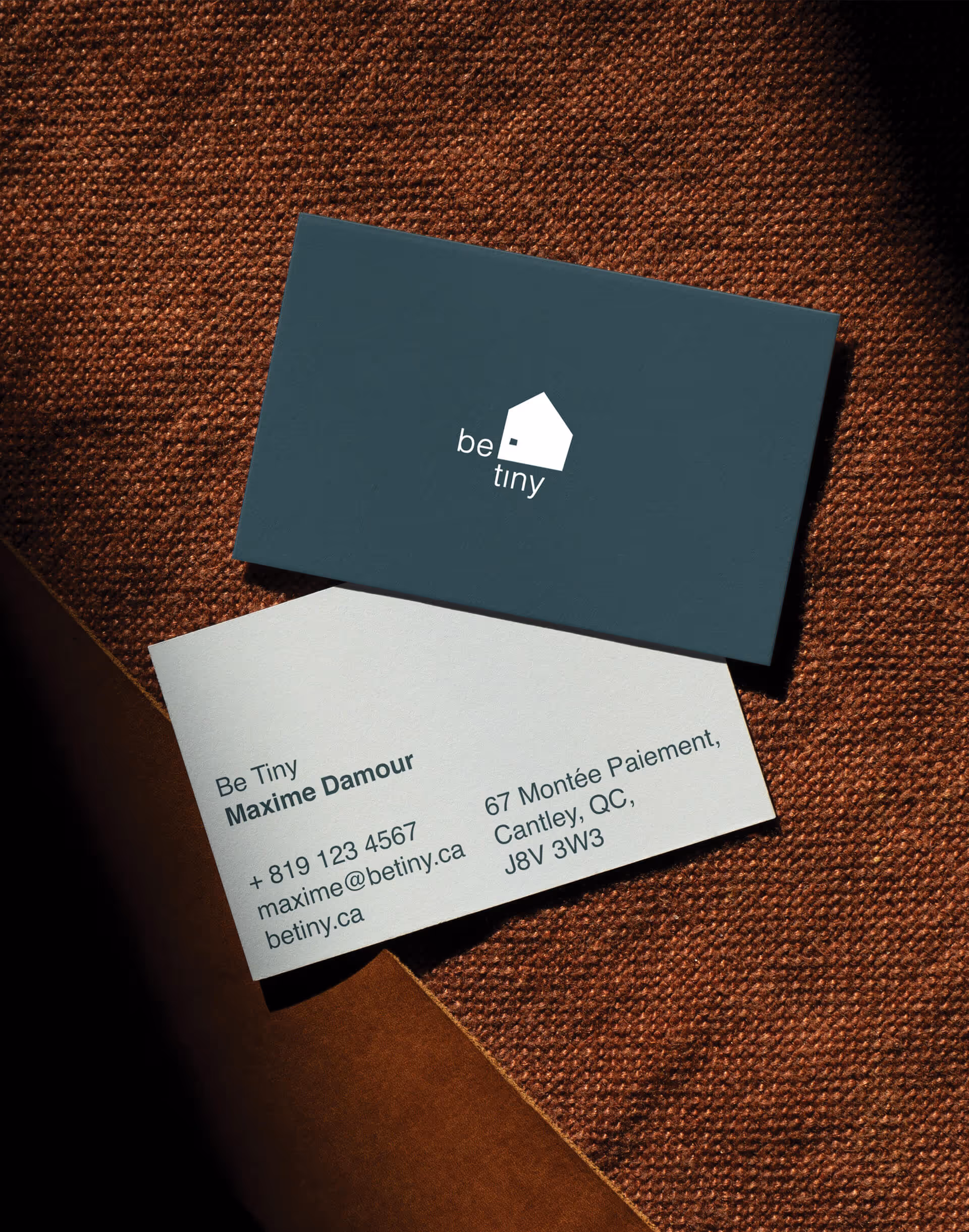 Two business cards on brown textured surface, one dark with house logo, one white with contact info.