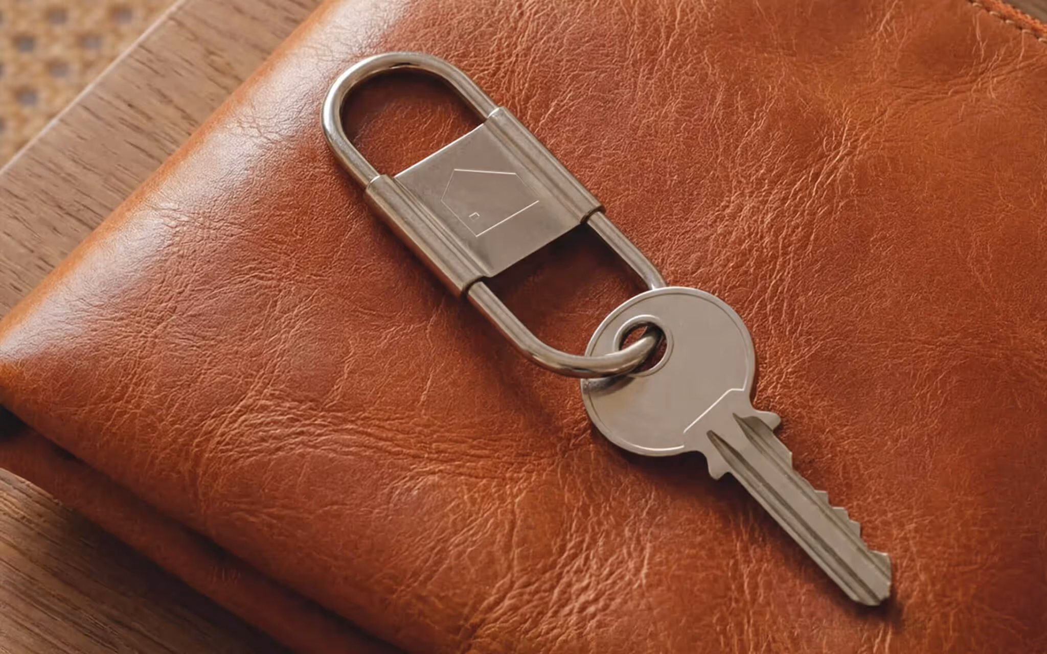 Silver key with a house icon keyring resting on a brown leather wallet on a wooden surface.