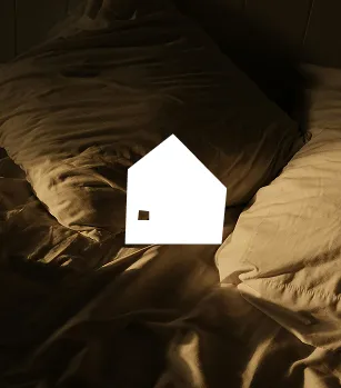 Soft rumpled bed sheets and pillow in warm, low light setting.