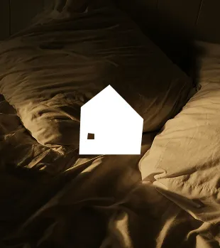 Soft dim-lit bed with rumpled brown sheets and pillows in warm brown tones.