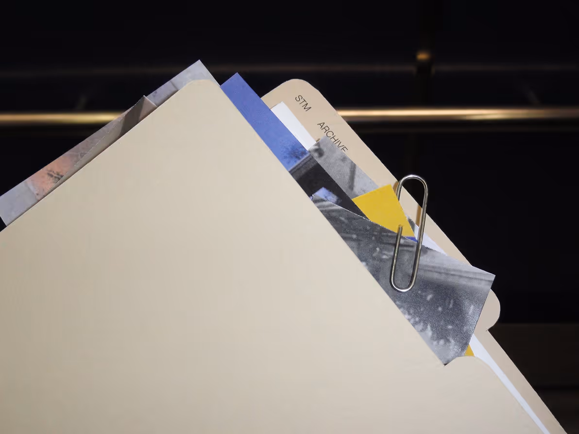 Beige file folder with papers and documents clipped by a silver paperclip against dark background.