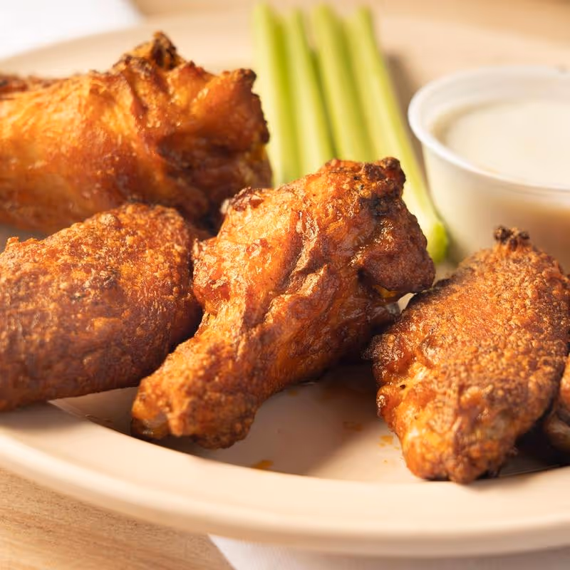 A plate of chicken wings with a side of celery and a dipping sauce.