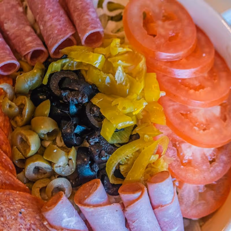 A bowl of food with a variety of ingredients including meat, tomatoes, olives, peppers, and mushrooms.