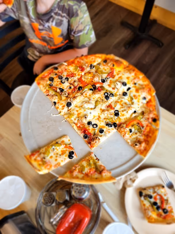 A pizza with olives, peppers, and cheese on a white plate.