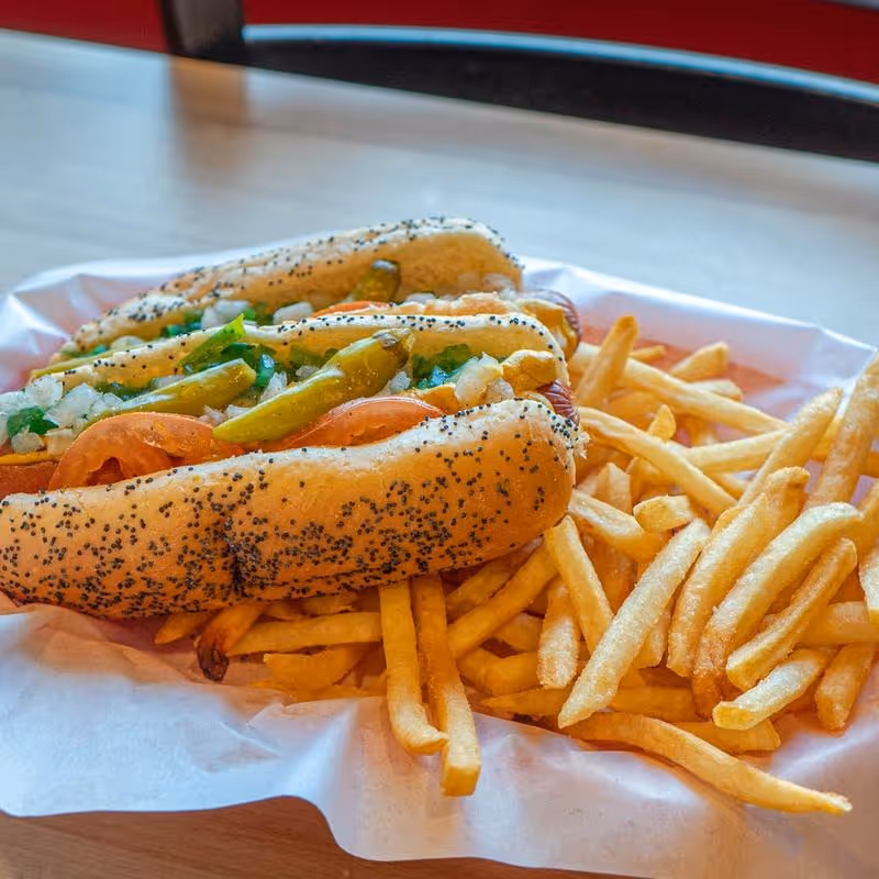A hot dog with onions and peppers on a bun with a side of french fries.