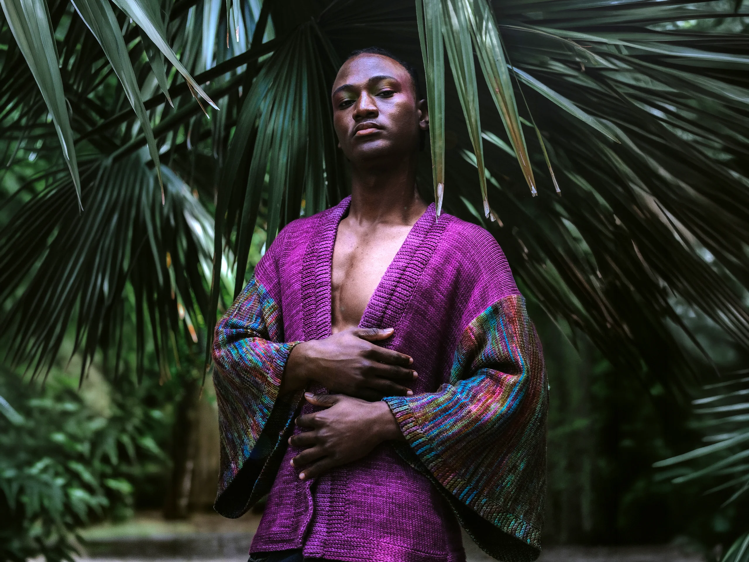 Kimono Symbiosis magenta porté bras croisés sous les palmes, manches multicolores tricotées main